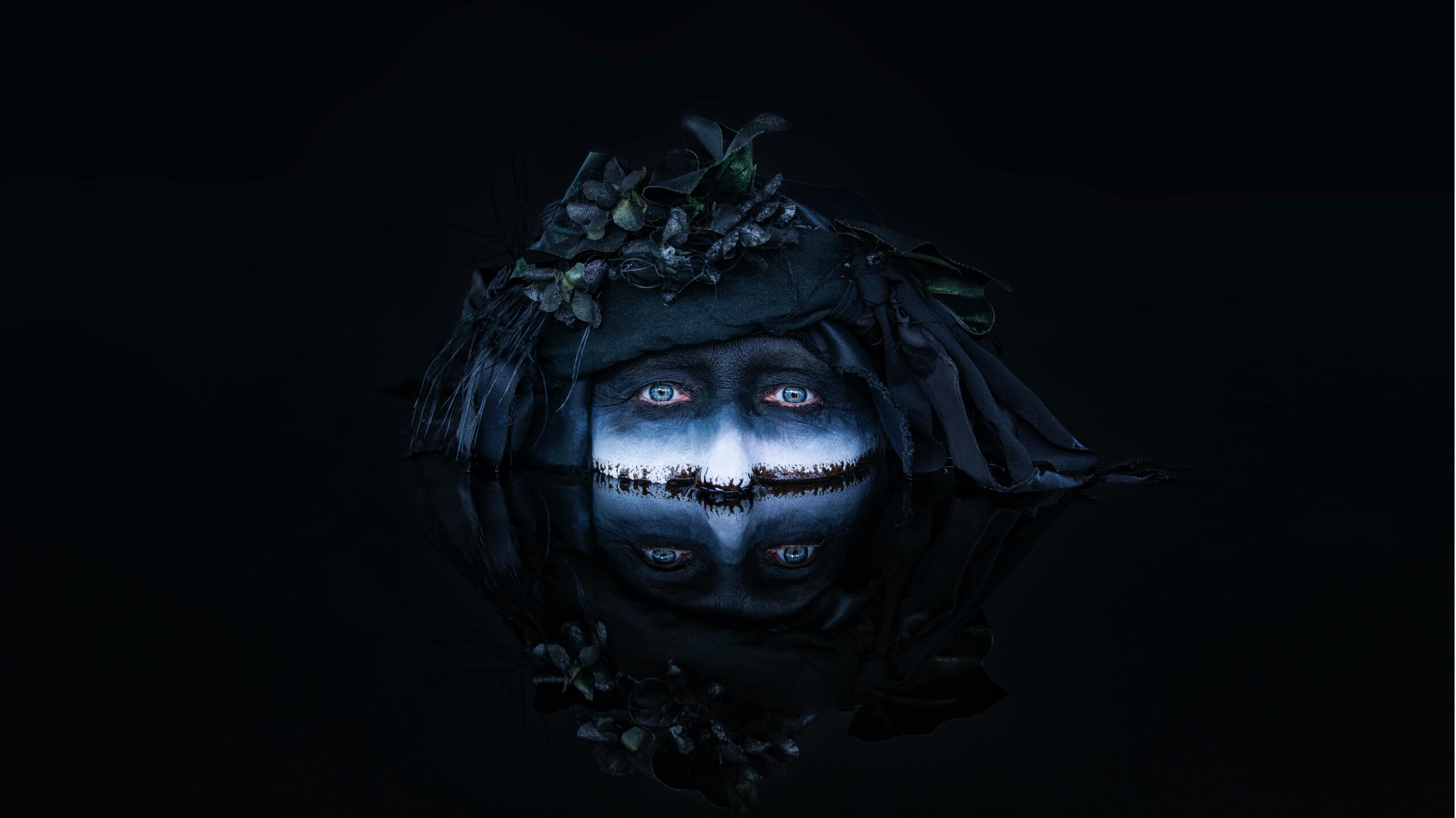 painted face submerged in oil on a dark background
