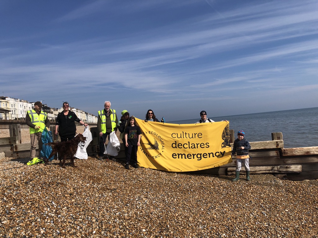 A group of people stand on Hasting beach holding a Culture Declares banner