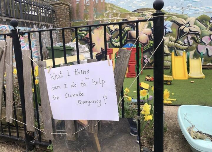 A piece of paper hanges on a gate and reads "what 1 thing can I do to help the Climate Emergency?"
