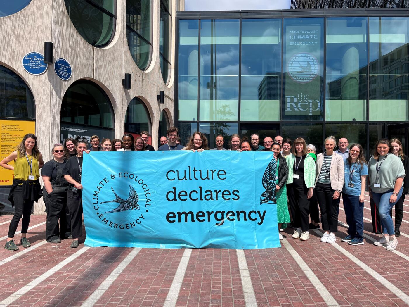 The Birmingham Rep team stand outside of their building holding a large blue Culture Declares banner