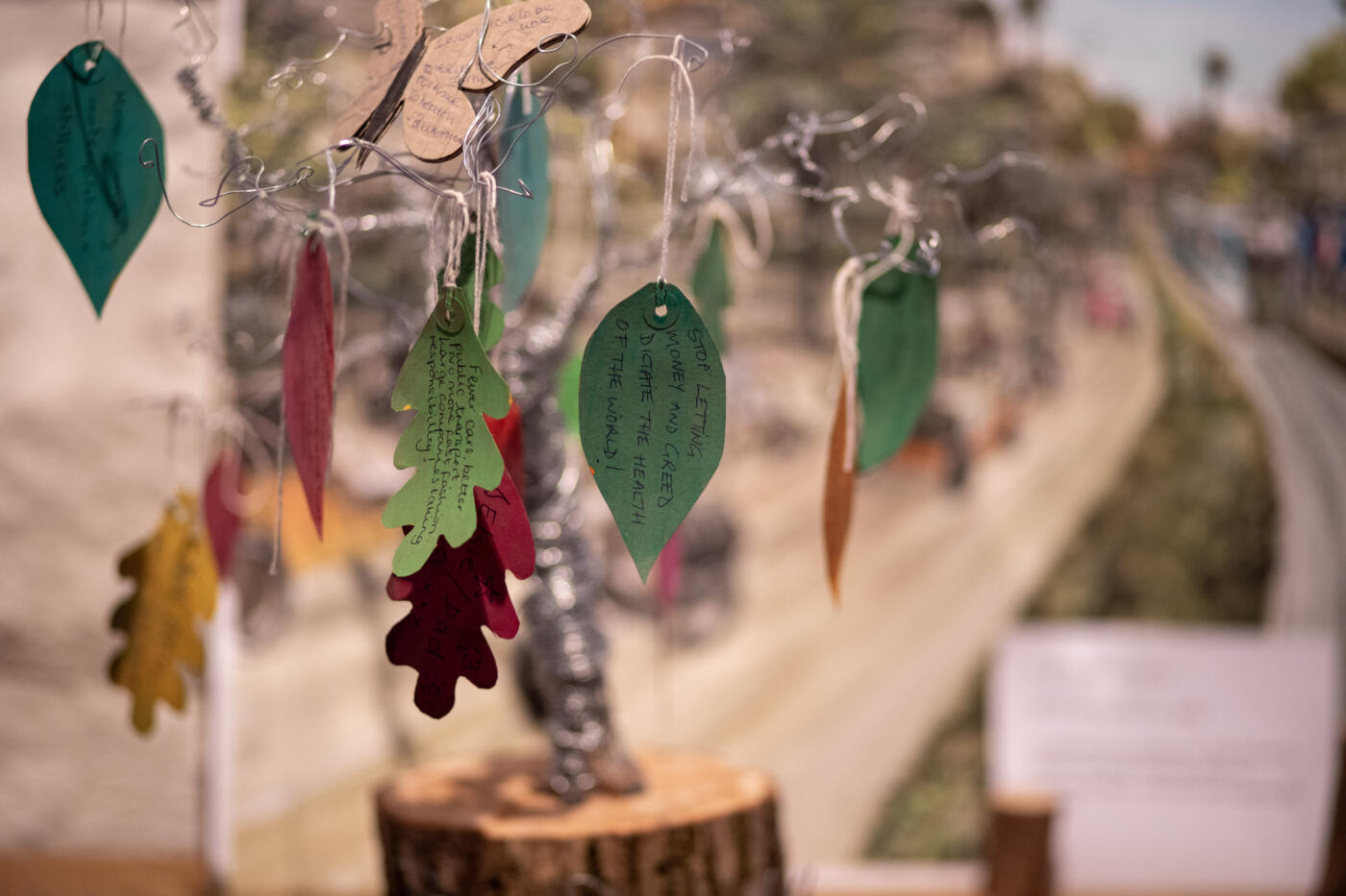 Paper leaves hang on a tree, with the clearest one reading "stop letting money and greed dictate the health of the world"
